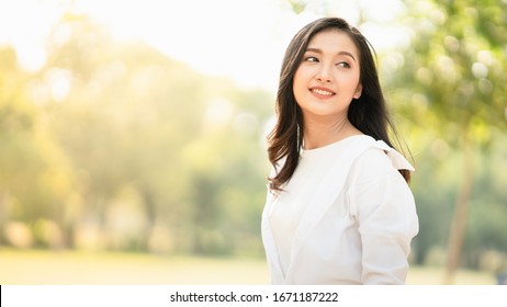 Portrait Of Young Asian Woman Wearing The White Shirt In Casual Style Smiling And Enjoy Life In The Natural Sunlight In The Park, Relaxing Moment, Enjoying The Nature, Mindful And Feel The Fresh Are.