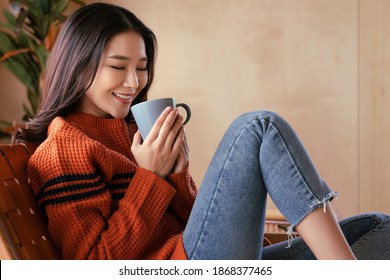 Portrait Of A Young Asian Woman Wearing A Sweater. She Inhaled The Scent And Drank The Winter Morning Coffee. She Smiles And Enjoys Being Relaxed At Home.