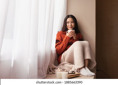 Portrait Of A Young Asian Woman Wearing A Sweater. She Inhaled The Scent And Drank The Winter Morning Coffee. She Smiles And Enjoys Being Relaxed At Home.