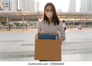 Portrait Of Young Asian Woman Wearing Covid-19 Protective Face Mask Holding Box Of Items After Being Laid Off From Job Due To Coronavirus