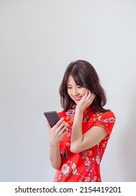 Portrait of a young asian woman wearing traditional cheongsam qipao dress using smartphone on white background.