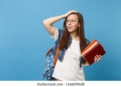 Portrait of young astonished woman student in glasses with backpack looking aside clinging to head holding school book isolated on blue background. Education in high school university college concept - Shutterstock ID 1166039638