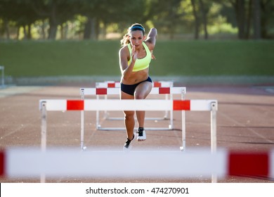 Portrait of young athlete jumping over a hurdle during training on race track. - Powered by Shutterstock