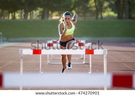 Portrait of young athlete jumping over a hurdle during training on race track.