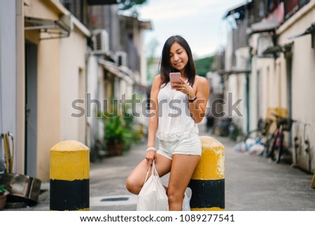 Portrait of a young, athletic, attractive and cute Chinese Asian girl using her smartphone on a street in Asia during the day. She is tanned, petite and relaxed. 
