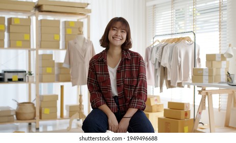Portrait young attractive asia female owner startup business look at camera work happy with carton box at home prepare delivery in sme supply chain, procurement, omnichannel ecommerce online concept.