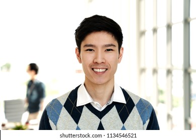 Portrait Of Young Attractive Asian Creative Man Smiling And Looking At Camera In Modern Office Feeling Confident And Positive. Headshot Of Chinese Male Employee, Entrepreneur Or College Student.