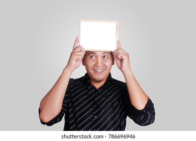 Portrait Of Young Attractive Asian Man Wearing Black Shirt, Holding And Showing Small Empty Copy Space Whiteboard Covering His Head, Smile Happy Expression