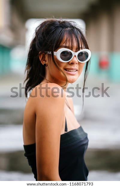 Portrait of a\
young and attractive Asian millennial teenager in trendy street\
fashion gazing directly at the camera. The girl is wearing cool\
sunglasses and smiling at the camera.\
