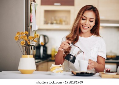 Portrait of young attractive Asian woman making herself breakfast and pouring fresh coffee