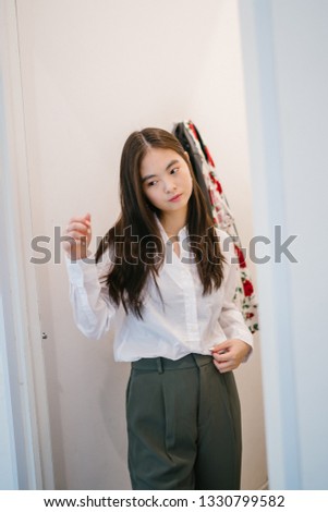 Portrait of a young, attractive and cute Chinese Asian girl trying out clothes in a fitting room. She is shopping for new clothes and is trying out a casual business outfit.