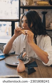 Portrait of a young attractive dark-haired woman eating a sandwich in a cafe. - Shutterstock ID 2301808241