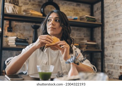 Portrait of a young attractive dark-haired woman eating a sandwich in a cafe. - Shutterstock ID 2304322193