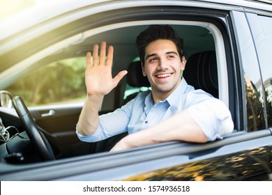 Portrait of young attractive handsome brunette man driving car and greeting somebody with hand. - Shutterstock ID 1574936518