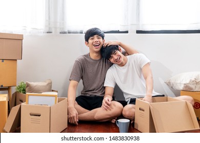 Portrait of young attractive happy asian couple man sitting at new home smiling to camera with carton package box storage to move in empty house. LGBTQ relationship and relocating concept - Powered by Shutterstock