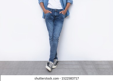 Portrait Of A Young Attractive Man In Blue Jeans Shirts With Blue Torn Jeans With Sneakers Posing In The Studio.