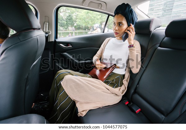 Portrait\
of a young, attractive Muslim woman commuting in a private\
limousine. She is wearing a turban and smartly but modestly dressed\
in the backseat and talking on her smartphone.\
