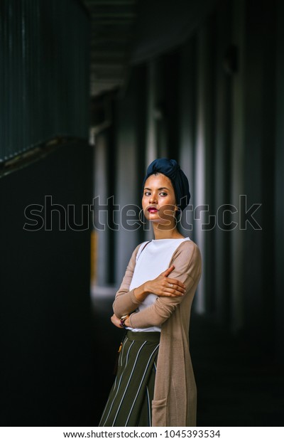Portrait of a young, attractive Muslim woman\
wearing a turban (hijab, head scarf) against a dark, textured,\
artistic background. She is of Asian, Saudi, Malay descent and is\
elegant and beautiful.