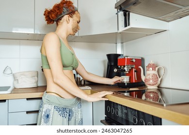 portrait young attractive positive woman, red-haired, curly, with bandage on hair, morning in cosmetic mask, in kitchen, preparing aromatic invigorating coffee in coffee maker - Powered by Shutterstock