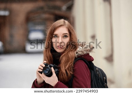 Portrait of young attractive redhead girl taking photographs with her dslr camera, Joyful and appealing ginger woman capturing city winter scenes with her camera.