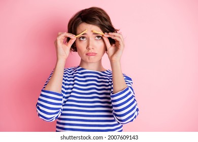 Portrait of young attractive sad upset unhappy girl look copyspace hold french fries on eyebrows isolated on pink color background