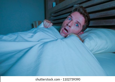 Portrait Of Young Attractive Scared Man In Fear And Panic Suffering Horror Nightmare Waking Up Suddenly At Night Lying On Bed In Dark Bedroom In Sleeping Disorder Concept