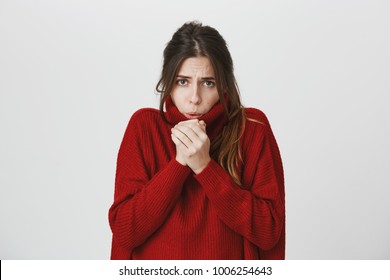 Portrait of young attractive stylish woman with brown hair in red winter sweater freezing, warming up hands over white background. Cute student feels cold as she ran from office to buy cup of coffee.