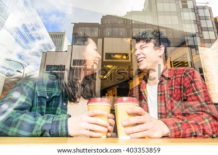 Portrait of a young attractive tourist couple behind coffee bar window. Two best friends having together fun in London drinking cappuccino. Boy and girl with glass reflection of buildings and skyline.