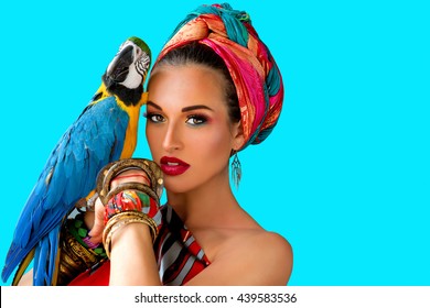 Portrait of young attractive woman in african style with ara parrot on her hand on colorful background