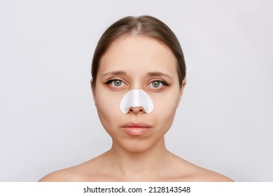 Portrait of young attractive woman with cleaning nose strips from blackheads or black dots on her skin isolated on a gray background. Acne problem, comedones. Enlarged pores on the face. Cosmetology
