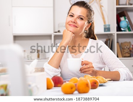 Portrait of young attractive woman with cup of tea sitting at table with peaches
