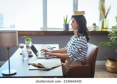 Portrait Of A Young Attractive Woman At The Desk With Books On Her Head, Sitting Straight, Working On Laptop. Education Concept Photo, Lifestyle. 