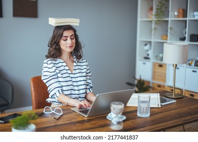 Portrait Of A Young Attractive Woman At The Desk With Books On Her Head, Sitting Straight, Working On Laptop. Education Concept Photo, Lifestyle. 