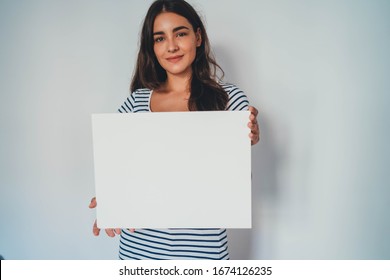 Portrait Of Young Attractive Woman Holding Blank Paper Against White Background, Hipster Girl Holding Blank Ad Poster With Copy Space For Text Message About Feminism Or Save Environment Poster