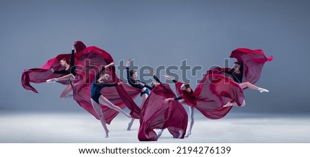 Portrait of young ballerina dancing with deep red clored fabric isolated over blue grey studio background. Flower bloom. Art style. Concept of classic ballet, inspiration, beauty, dance, creativity