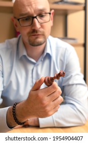 Portrait Of Young Bearded Business Man With Glasses With Perplexity Looking At Chess Queen Holding In Hand On Blur Background. Solution Problem. Disappointed Or Annoyed Look. Lost Game Or No Decision