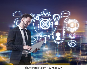 Portrait Of A Young Bearded Businessman Standing With His Laptop Against A Night City Panorama With A Buisness Idea Sketch In The Air.