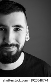 Portrait Of A Young Bearded Man On A Gray Background. The Young Man Smiles. Black And White Photo.