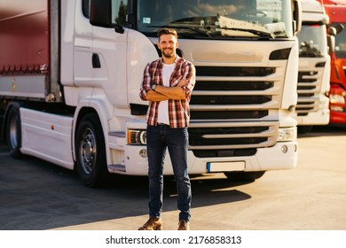 Portrait of young bearded man standing by his truck. Professional truck driver with crossed arms standing by semi truck vehicle. - Shutterstock ID 2176858313