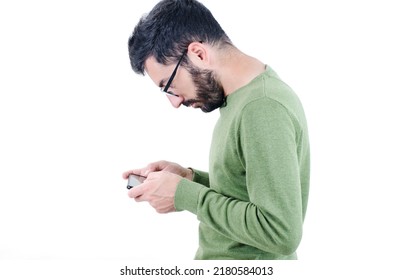 Portrait Of A Young Bearded Man Wearing Sweater Standing Isolated Over White Background, Using Mobile Phone. Crooked Man With Muscle Strength Imbalance. Incorrect Spine Curvature Caused By Bad Posture