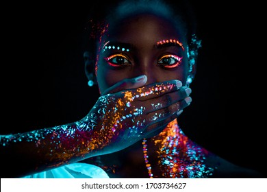 Portrait Of Young Beautiful African Woman With Fluorescent Prints On Face And Closed Mouth. Fluorescent Prints Glowing On Ultra Violet Rays, Keep Silence Gesture