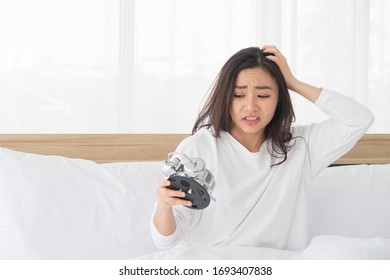 Portrait Of Young Beautiful Asian Bad Moody Woman Shocked Looking At The Clock And Sitting In White Bed While Wake Up Late In The Morning.