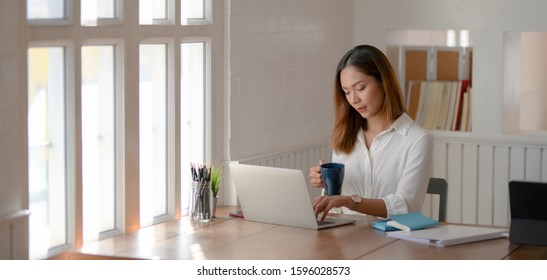 Portrait of young beautiful asian businesswoman working on her project and drinking a coffee  - Shutterstock ID 1596028573