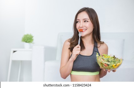 Portrait Of Young Beautiful Asian Girl In Sportswear Holding A Glass Bowl Of Salad Fork In Her Hands. Concept Of Vegan Woman Eating Healthy Food And Tasty Food Health Care Medical Plant Base Concept.