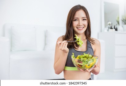 Portrait Of Young Beautiful Asian Girl In Sportswear Holding A Glass Bowl Of Salad Fork In Her Hands. Concept Of Vegan Woman Eating Healthy Food And Tasty Food Health Care Medical Plant Base Concept.