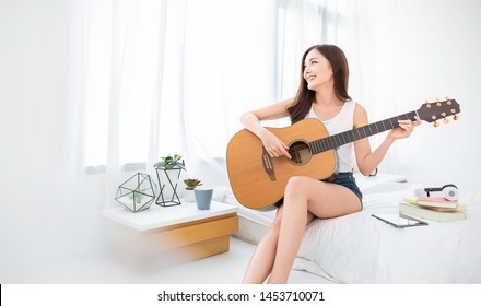 Portrait of young beautiful asian woman playing guitar music, sing and dance in bedroom. Smile happy asian girl relaxing knowledge education university woman lifestyle, back to school concept - Powered by Shutterstock