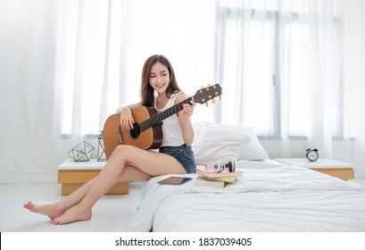 Portrait of young beautiful asian woman playing guitar music, sing and dance in bedroom. Smile happy asian girl relaxing, knowledge education university, woman lifestyle, back to school concept - Powered by Shutterstock