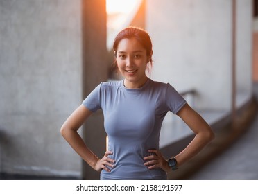 Portrait Young Beautiful Asian Woman Wearing Sportswear Standing Pose Smiling In The City At Sunrise. Cheerfully Sporty Female Workout And Exercise In The Morning.