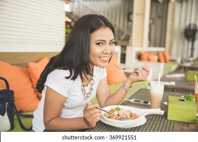 A Portrait Of A Young Beautiful Asian Woman In A Restaurant, Enjoying Her Food