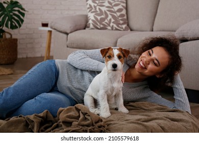 Portrait of young beautiful black woman with her adorable wire haired Jack Russel terrier puppy at home. Loving girl with rough coated pup having fun on the couch. Background, close up, copy space.